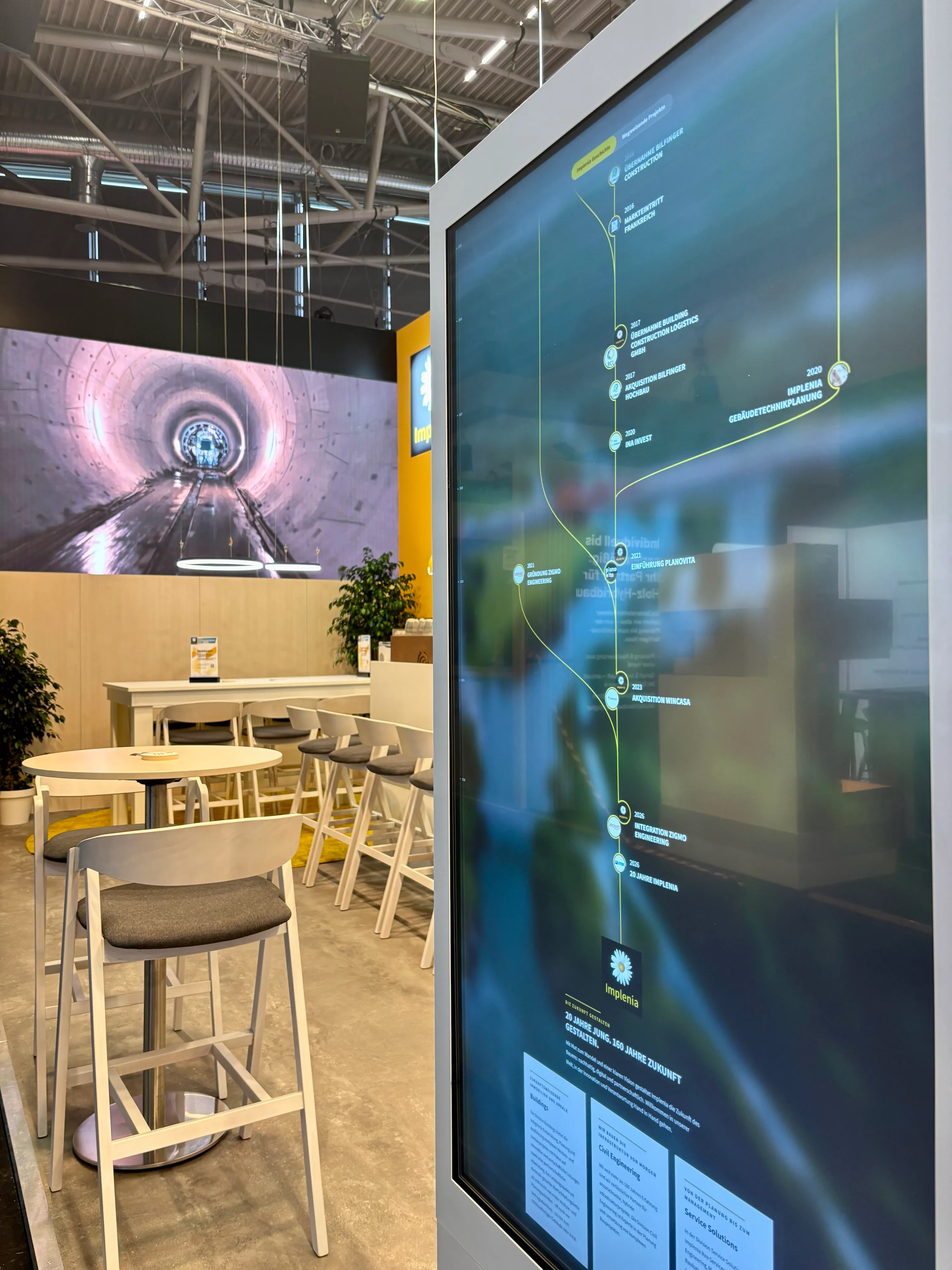 EXPO REAL 2026 in München: Eine digitale Stele am Messestand von Implenia zeigt die vertikale Zeitleiste